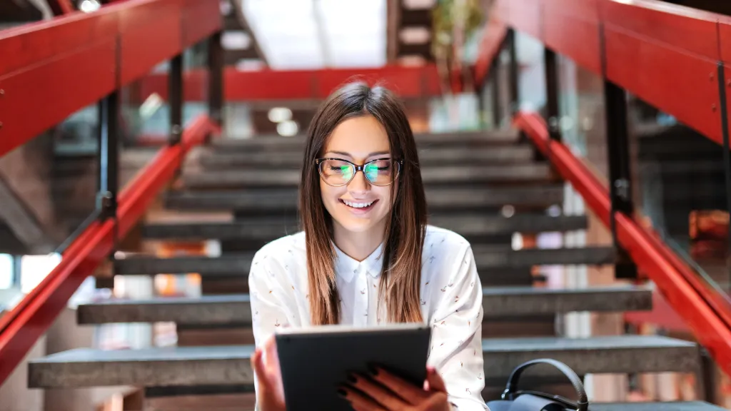 Woman sitting on stairs reading something on a tablet.