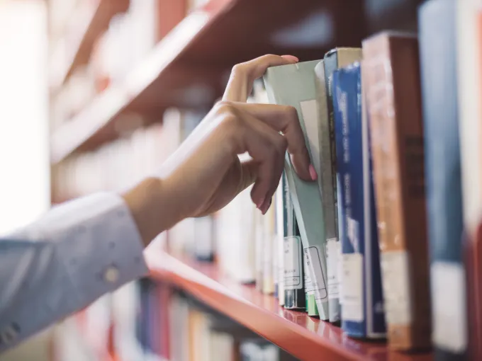 A hand pulling out a book on a library book shelf.