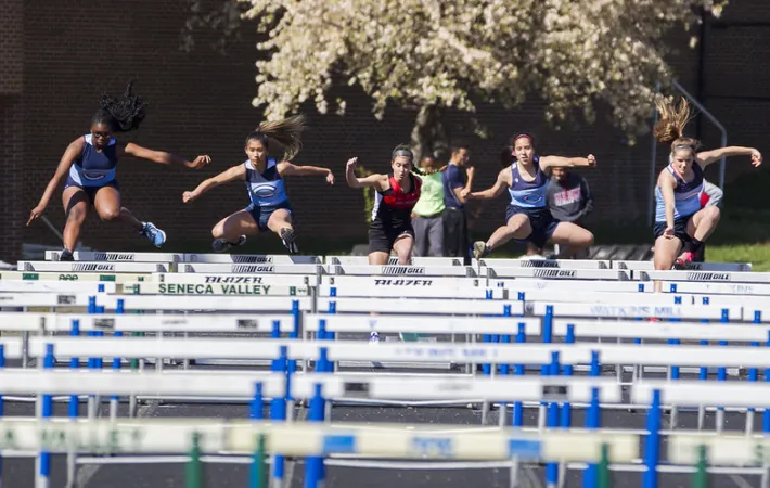A group of students leaping over hurdles at a track meet.